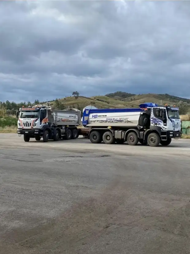 Due autocarri a quattro assi con cassone ribaltabile della flotta aziendale fermi su un piazzale